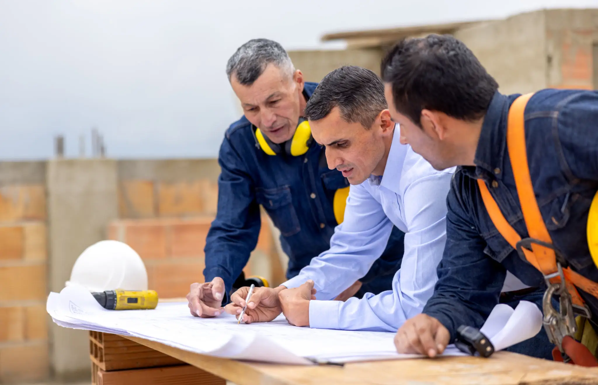 Three men reviewing construction plans on a building site.