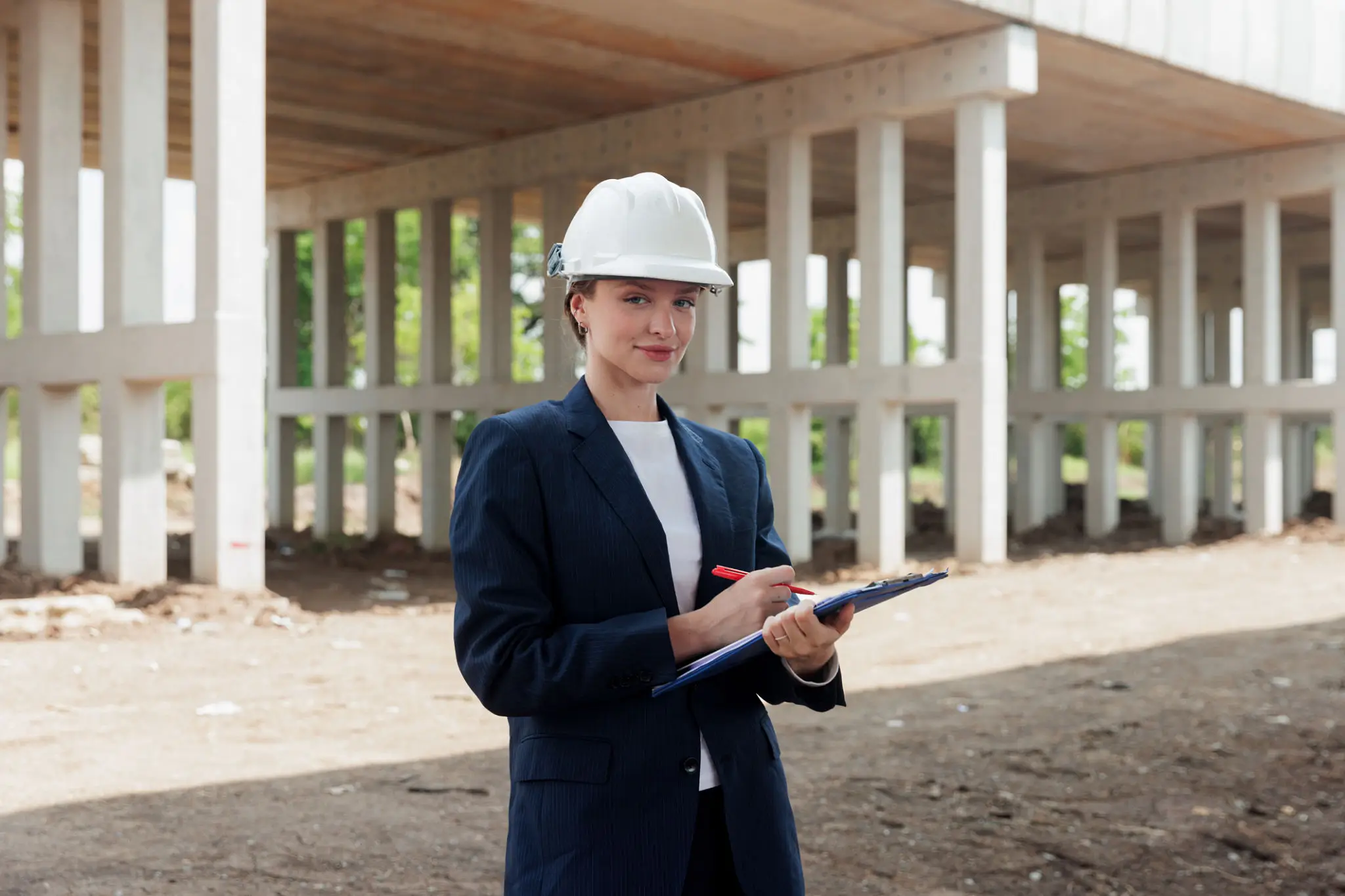 Engineer in a hard hat inspecting a construction site with a clipboard.