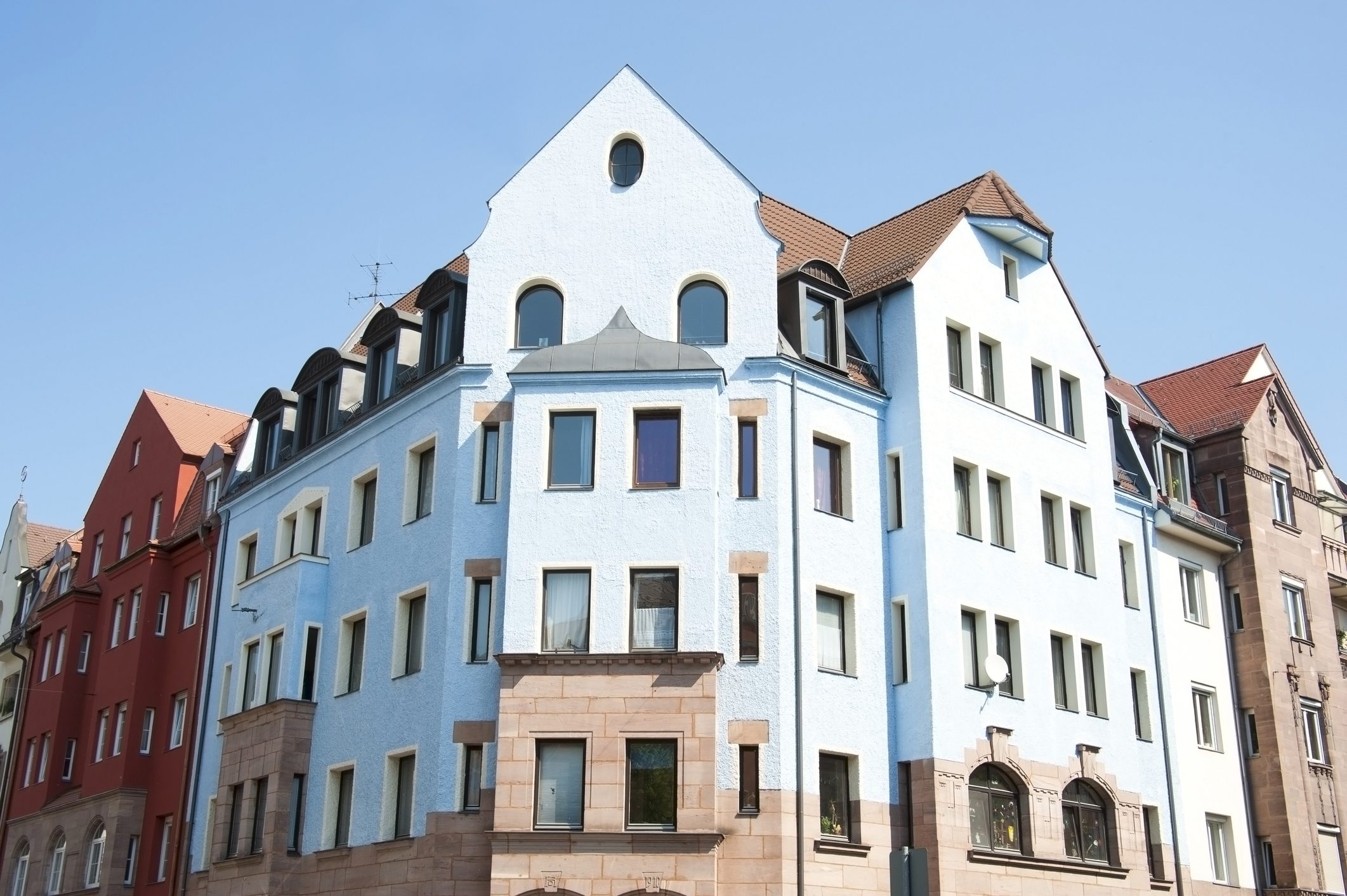 A multi-story white building with a brown roof under a blue sky.