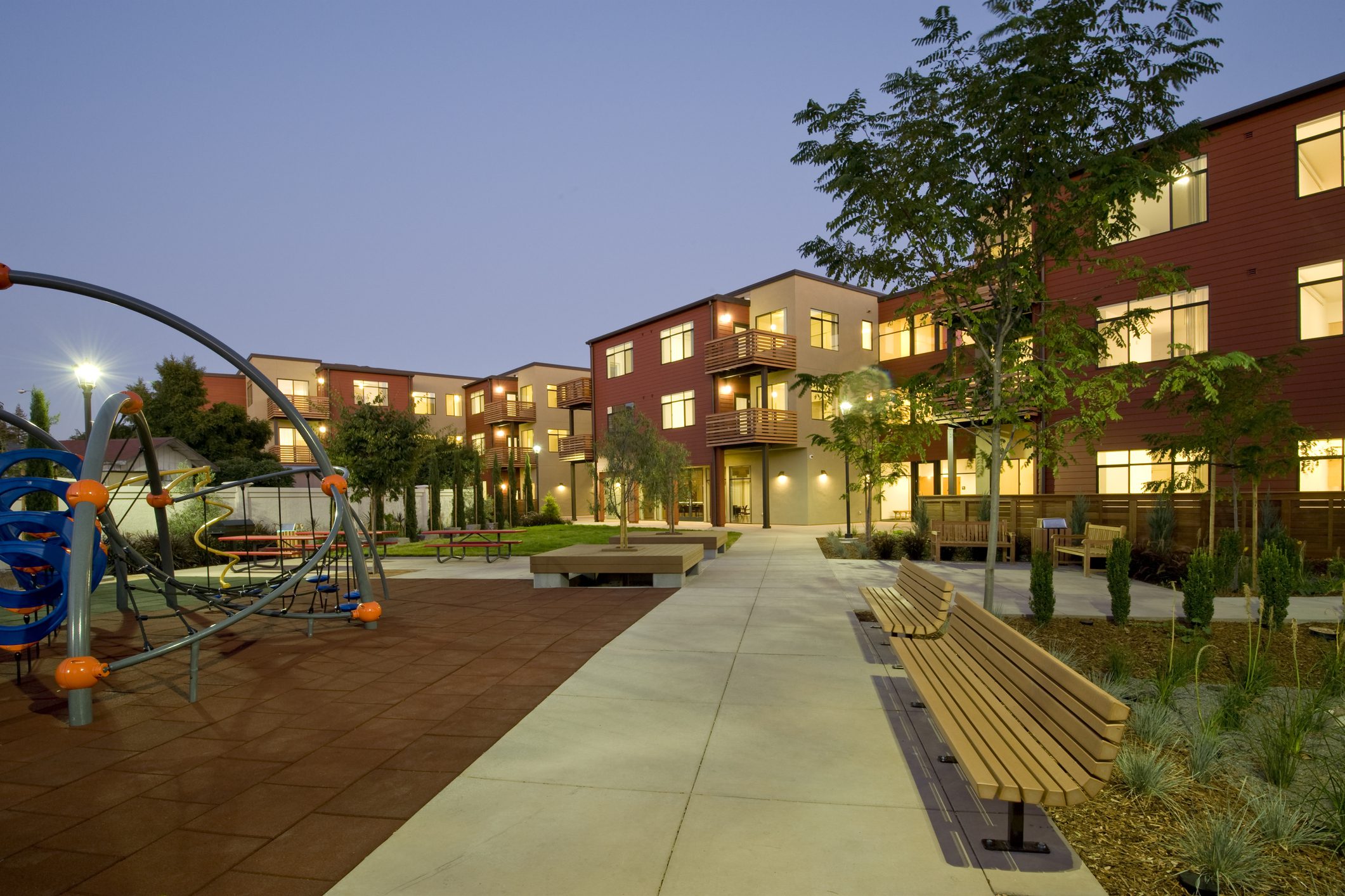 Well-lit modern building with courtyard and playground at dusk.