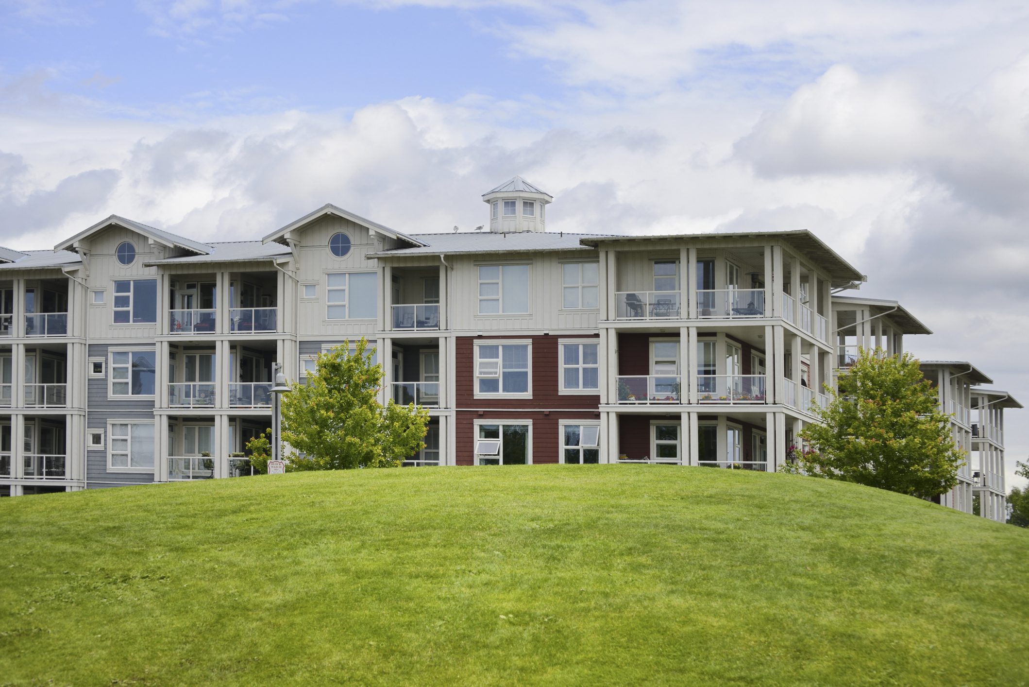 A large, modern three-story building with balconies and a green lawn.