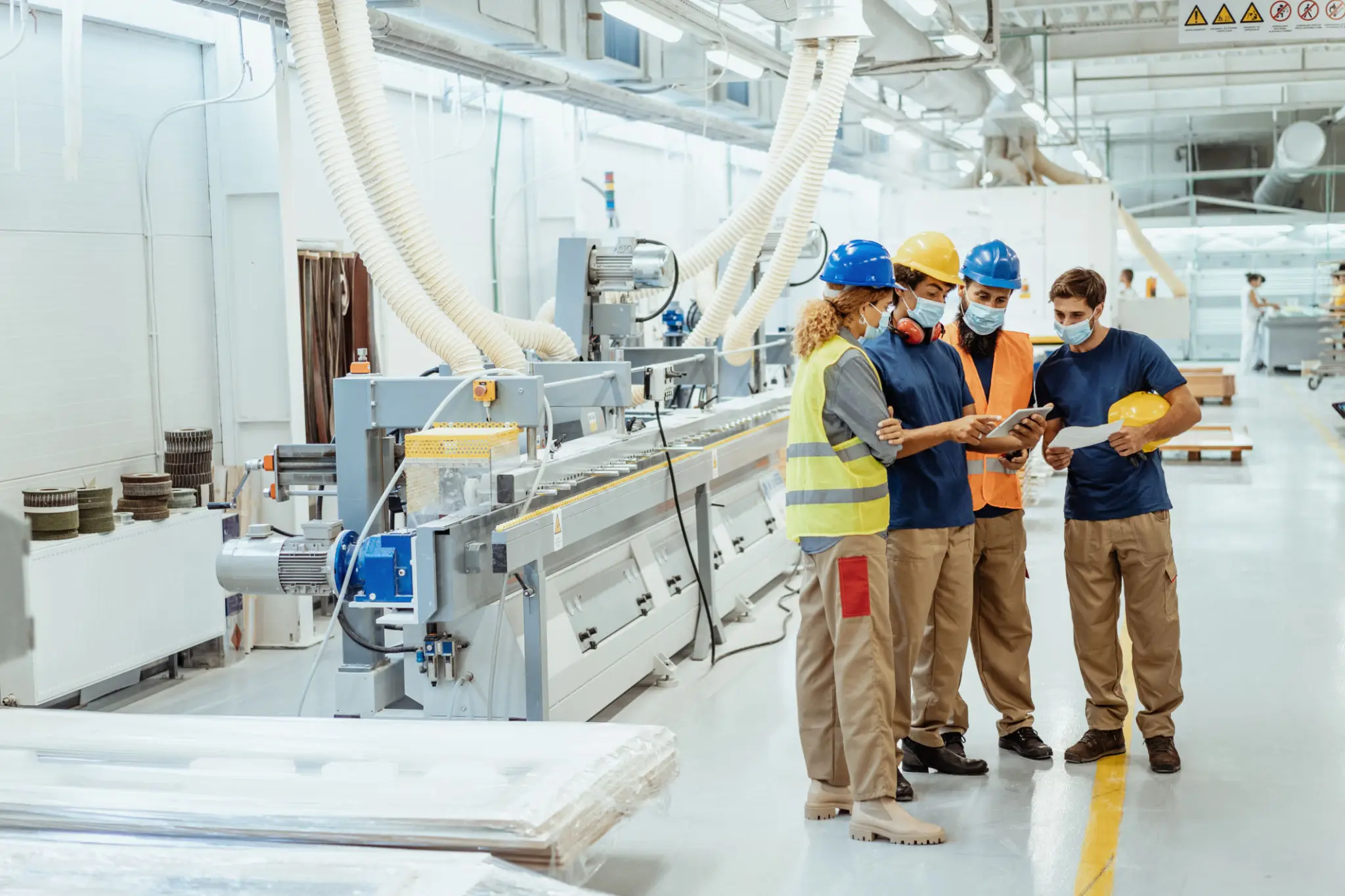 Workers in helmets discussing near machinery in a factory.