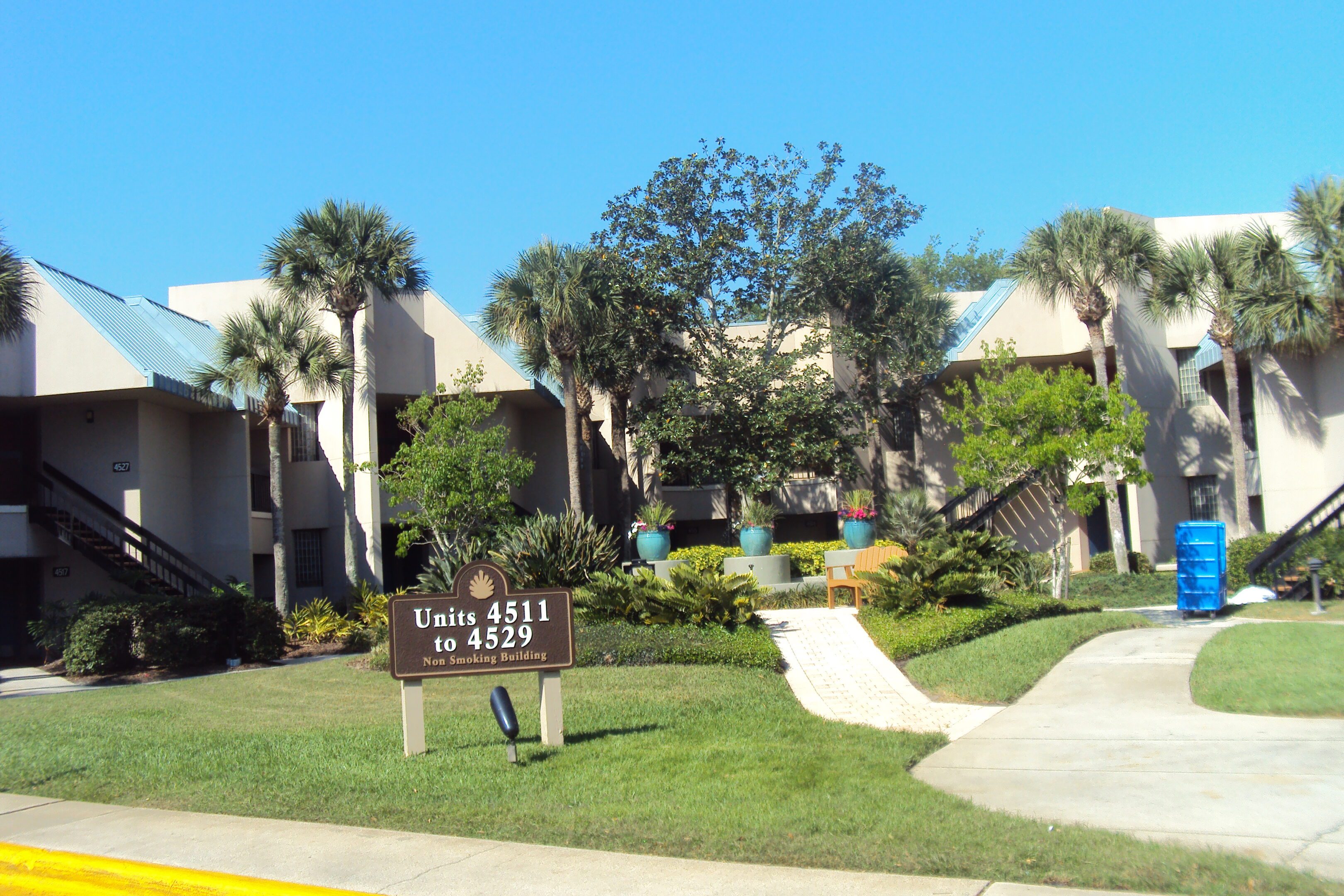 Entrance to a community with manicured lawns and palm trees under a clear sky.