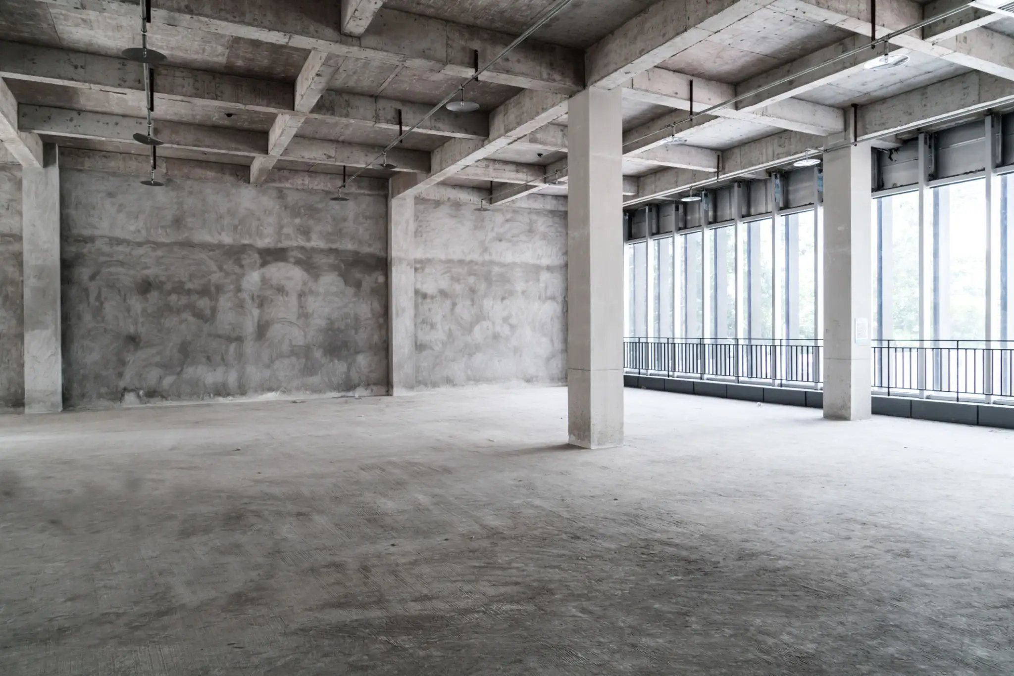 Empty industrial-style concrete room with large windows and pillars.
