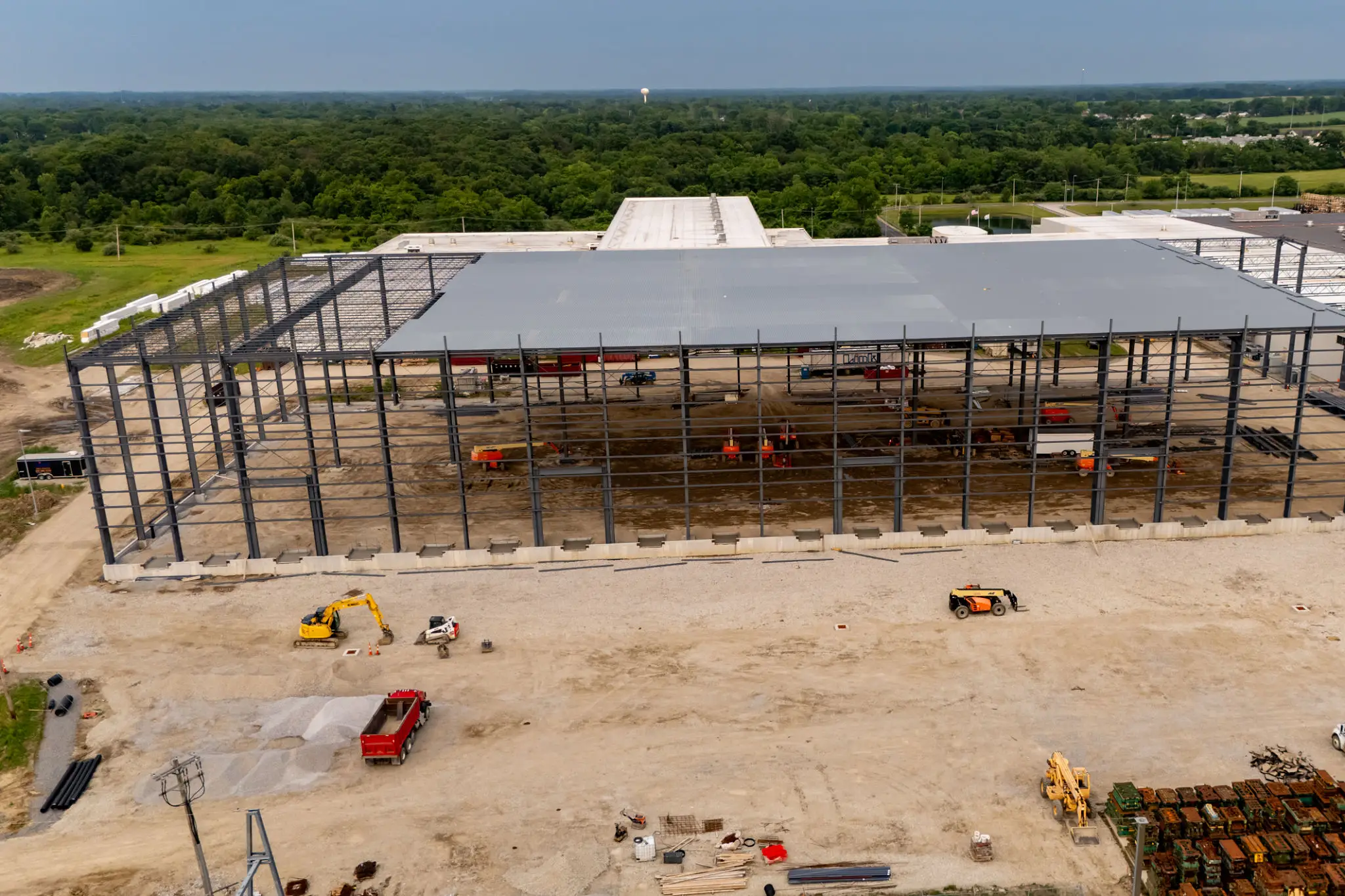Construction site with steel framework and vehicles on a dirt ground.