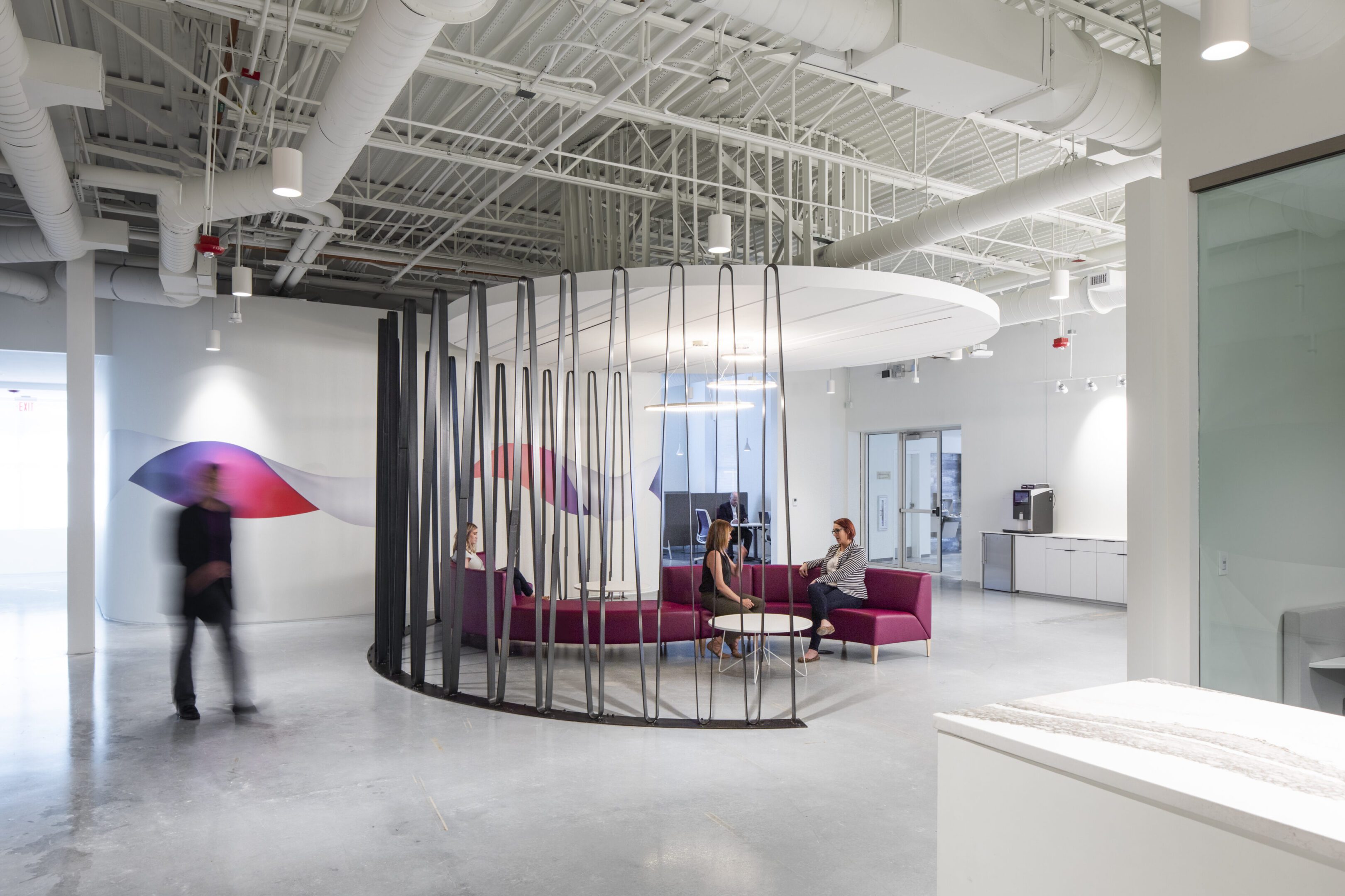 Modern office lounge with curved metal partition and casual seating.