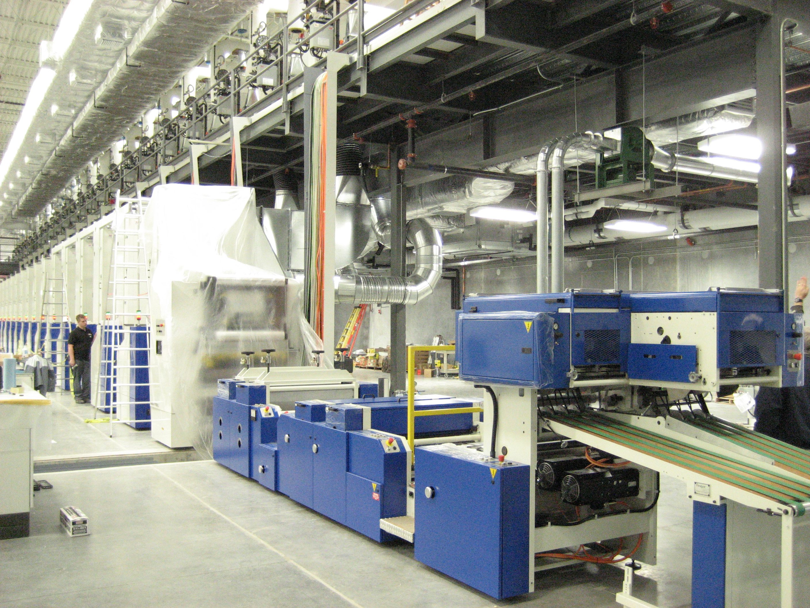 Industrial machinery setup inside a factory with blue equipment and ventilation pipes.